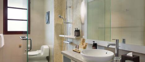 Un baño moderno con cabina de ducha de vidrio, inodoro, lavabo con un espejo grande y artículos de aseo en la encimera.