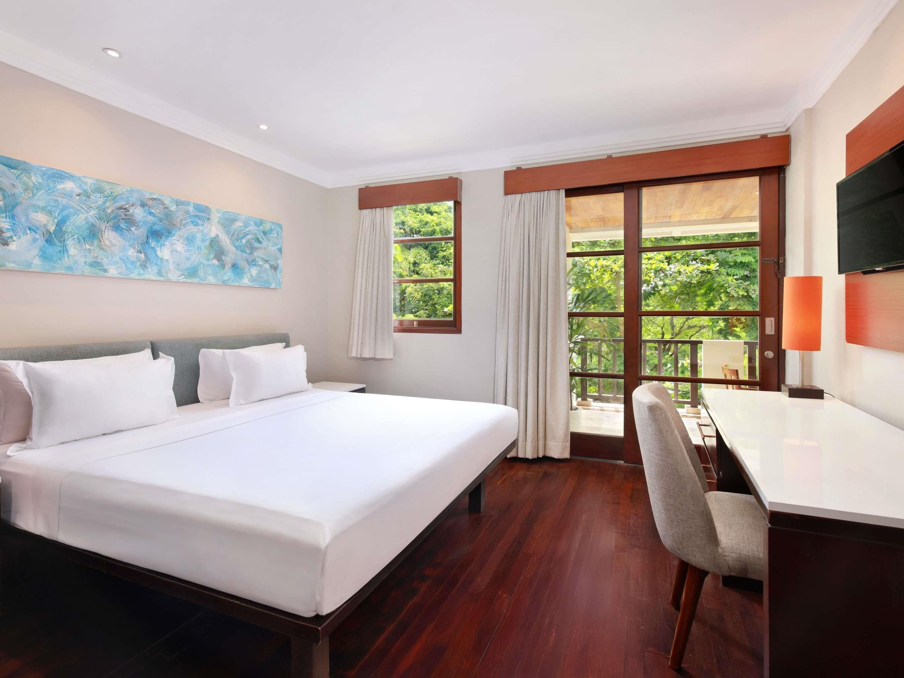 Ein Hotelzimmer mit einem großen Bett, einem Schreibtisch, einem Stuhl, einem Fernseher und einem Bild an der Wand.