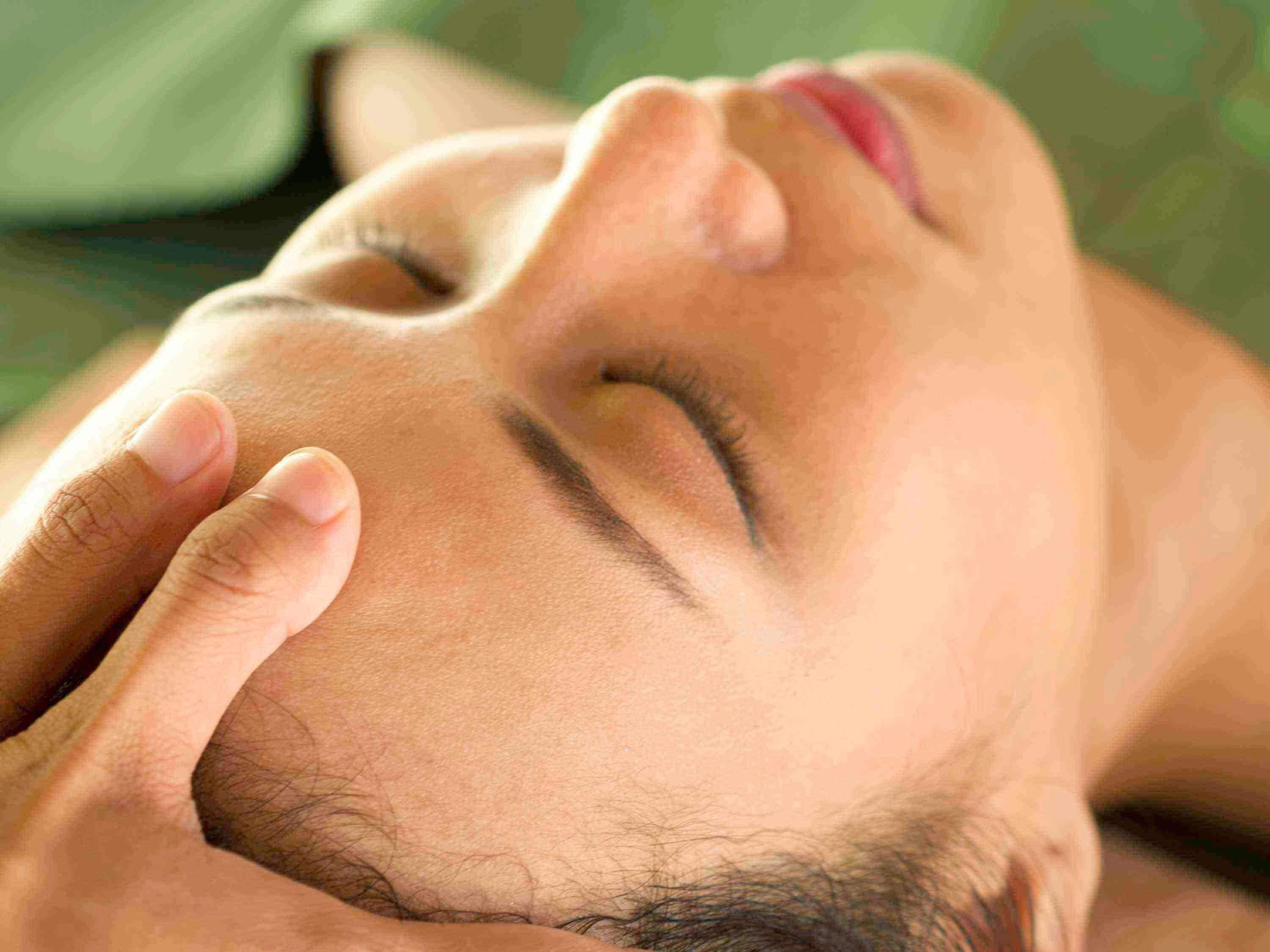 A close-up of a person's face with a hand gently touching their forehead.