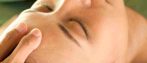 A close-up of a person's face with a hand gently touching their forehead.