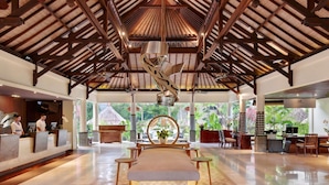 A spacious lobby with a high ceiling, a reception desk, seating area, and a view of greenery outside.