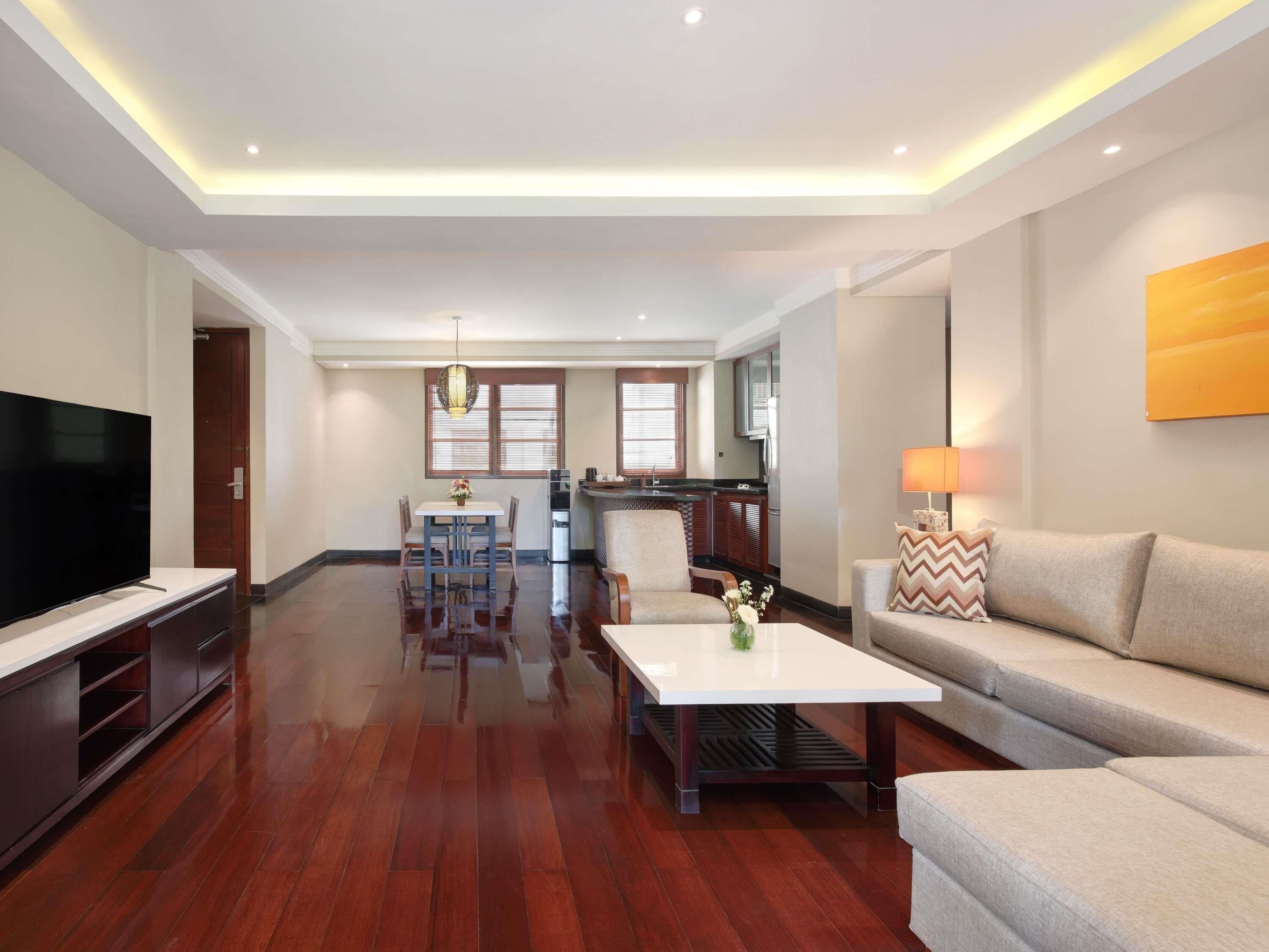 A modern living room with a flat-screen TV, a sofa, a coffee table, and a dining area with a table and chairs.