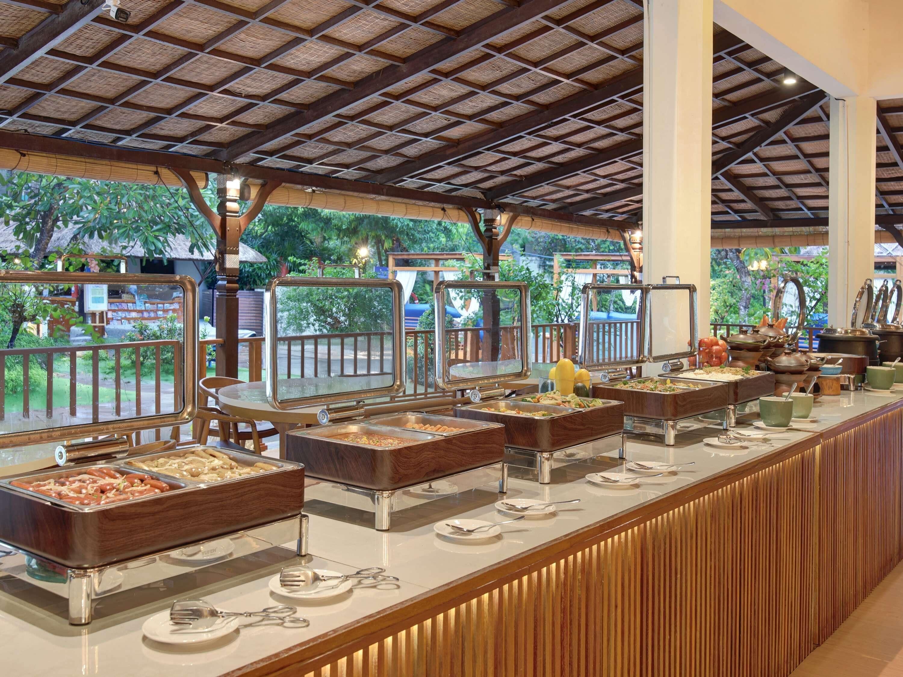 A buffet setup with multiple food stations, a wooden counter, and a thatched roof structure.