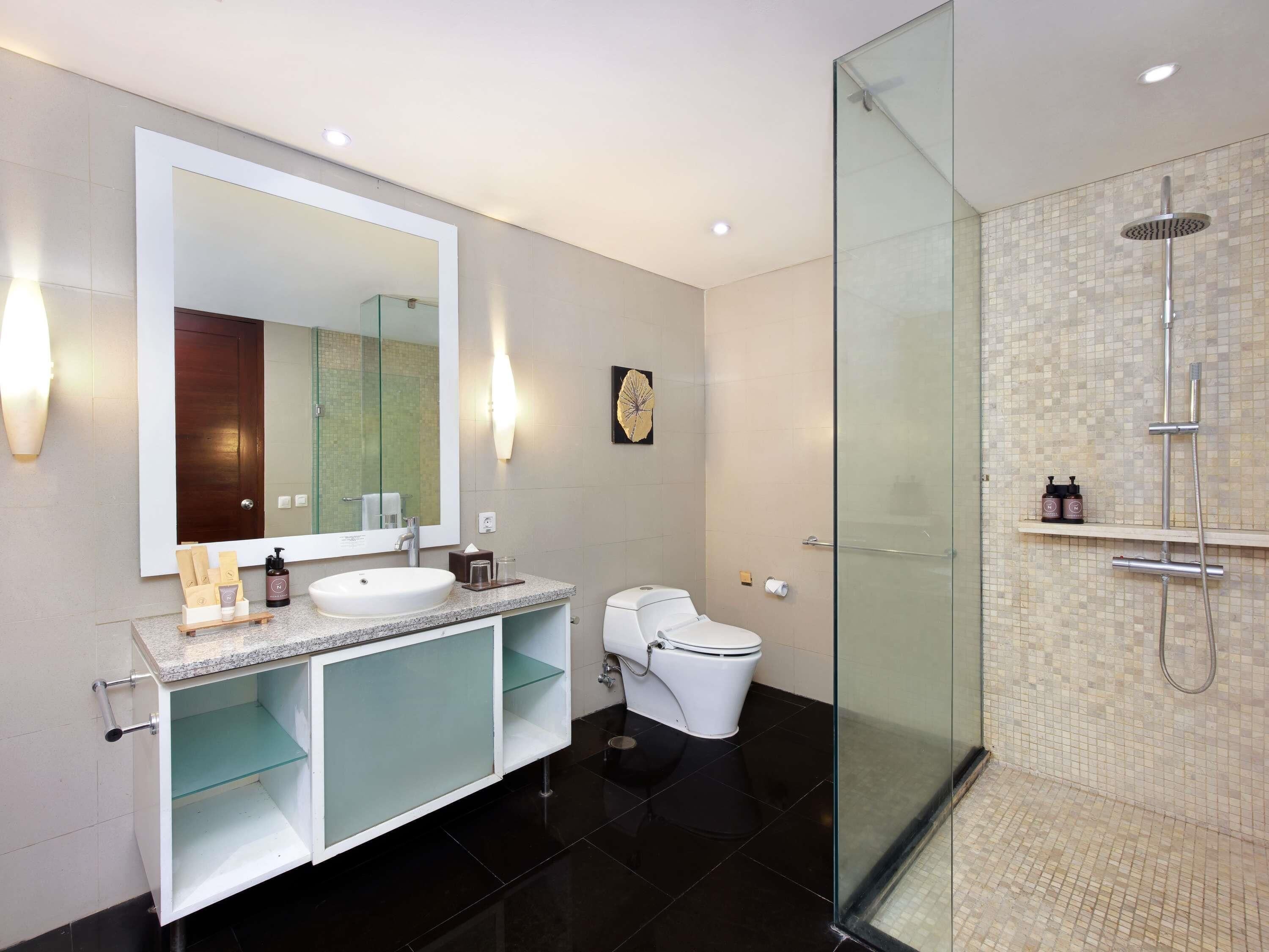 Un baño moderno con un espejo grande, un lavamanos, un inodoro y una ducha con mampara de vidrio.
