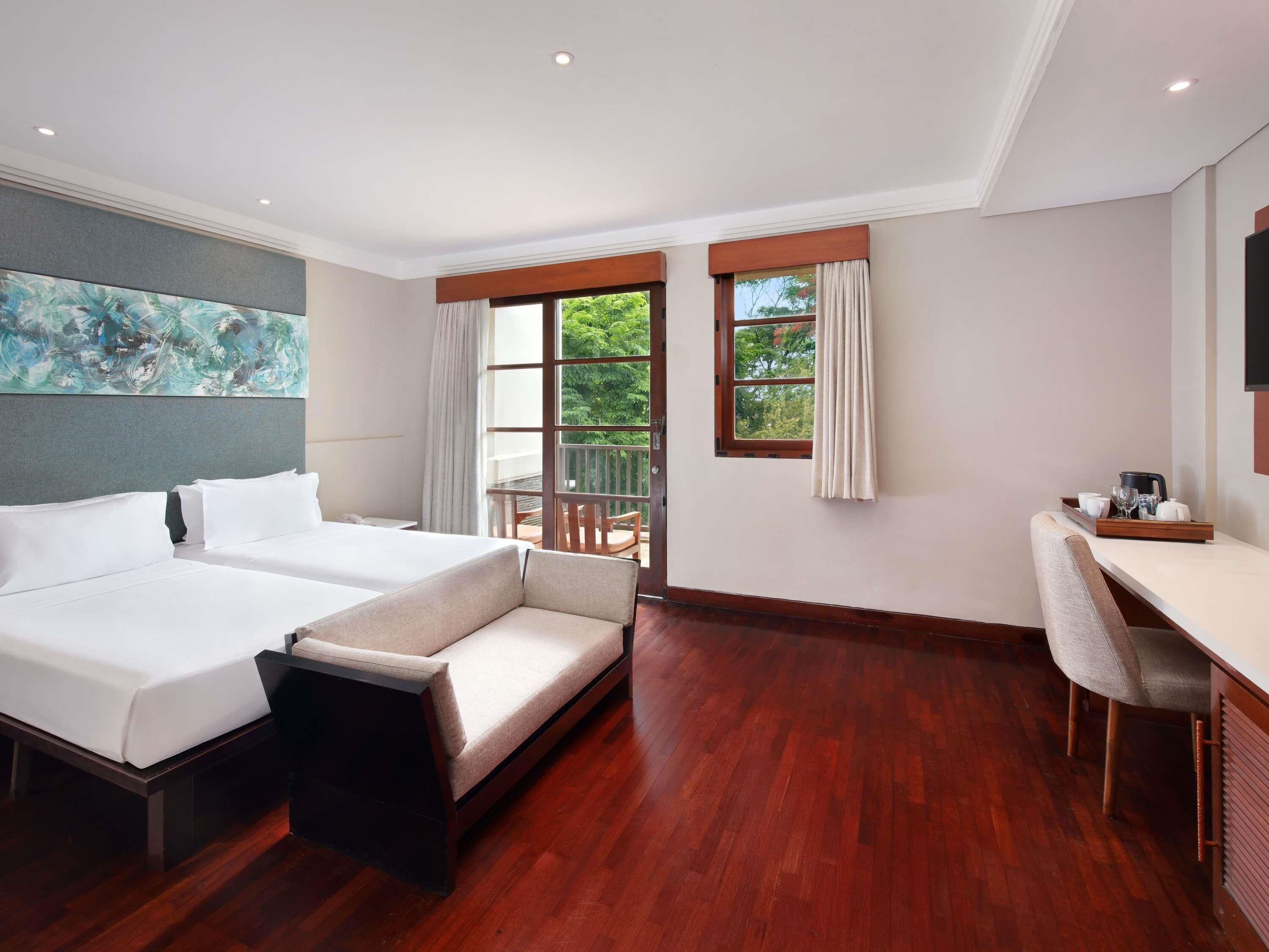 Ein Hotelzimmer mit einem großen Bett, einem Sofa, einem Schreibtisch und einem Balkon mit Vorhängen.