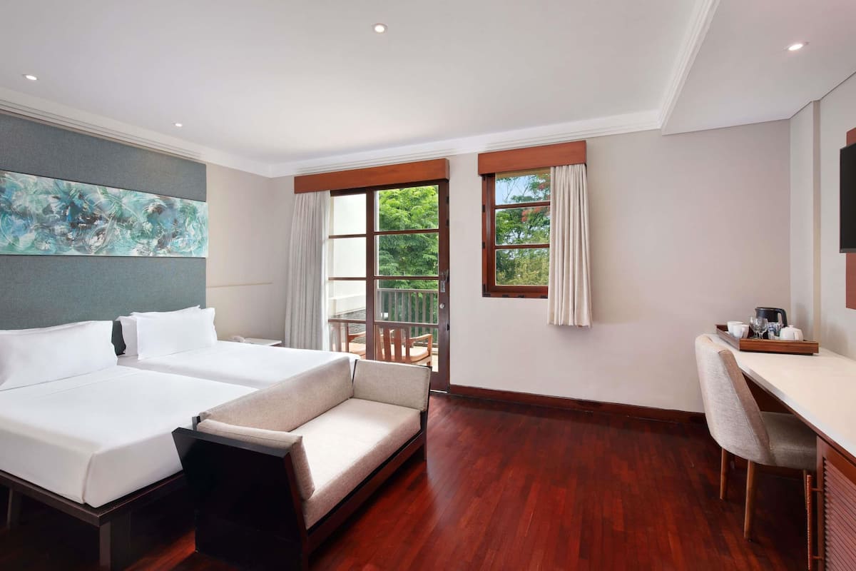 Ein Hotelzimmer mit einem großen Bett, einem Sofa, einem Schreibtisch und einem Balkon mit Vorhängen.