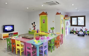 Ein helles Kinderzimmer mit Fernseher, Spielbereich und farbenfrohem Mobiliar.
