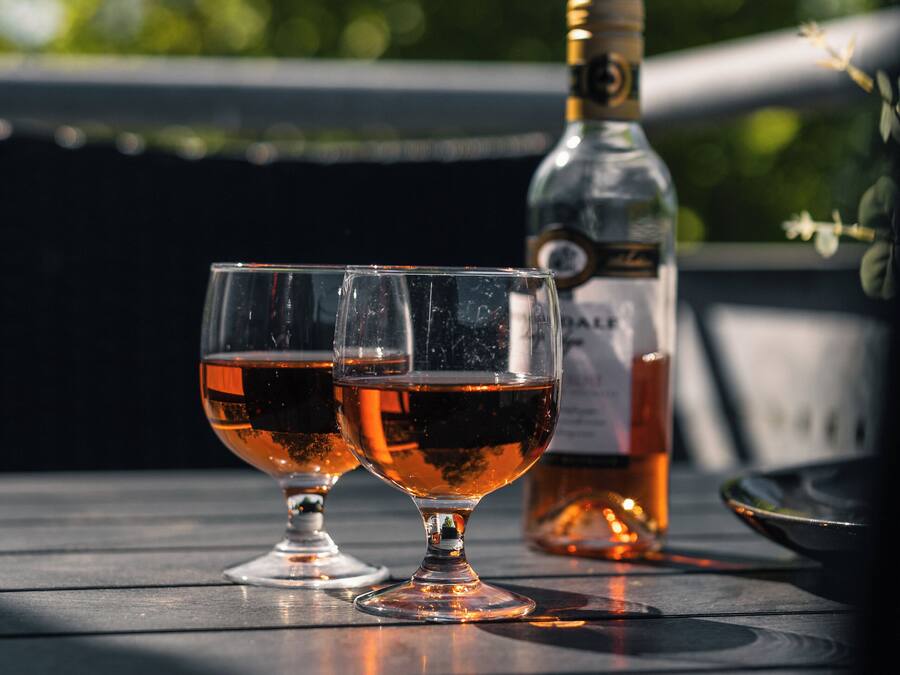 Two glasses of red wine on a wooden table with a bottle in the background.
