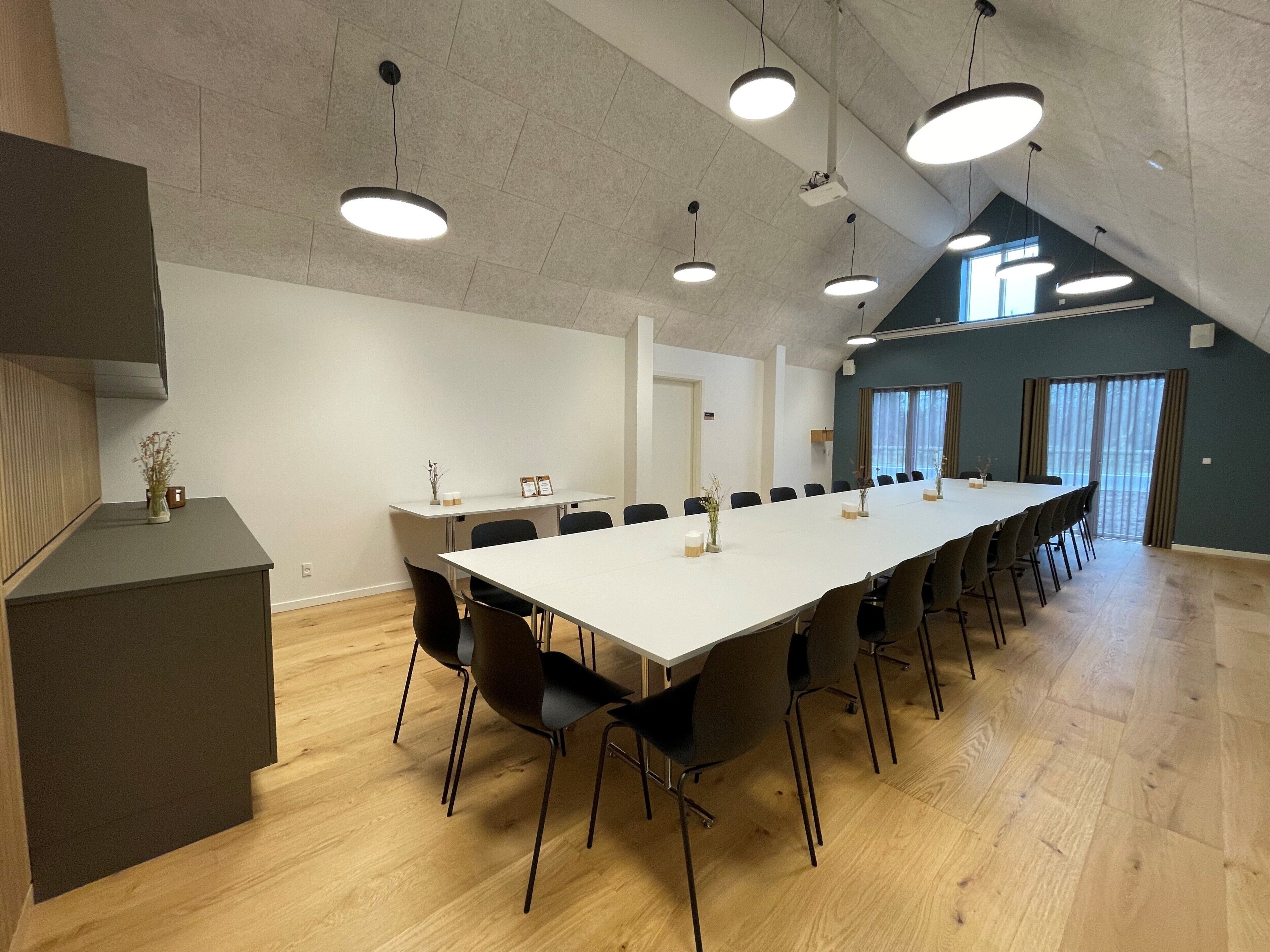 Een vergaderzaal met een lange tafel, stoelen en hanglampen.