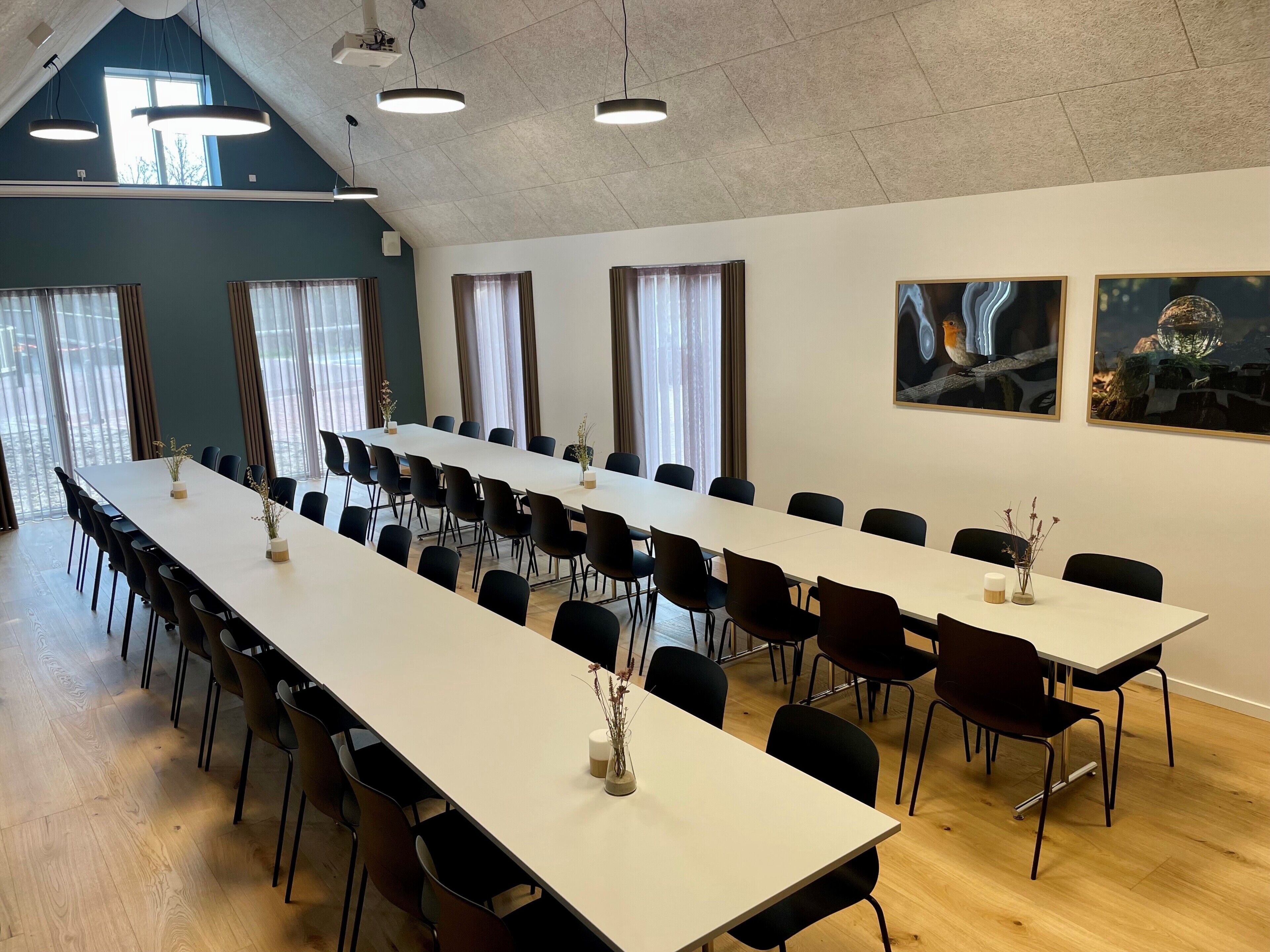 Un salón de conferencias con una larga mesa, sillas negras y ventanas grandes con cortinas.