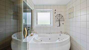 Une salle de bain moderne dotée d’une grande baignoire îlot, d’une douche à parois de verre et d’une fenêtre laissant entrer la lumière naturelle.