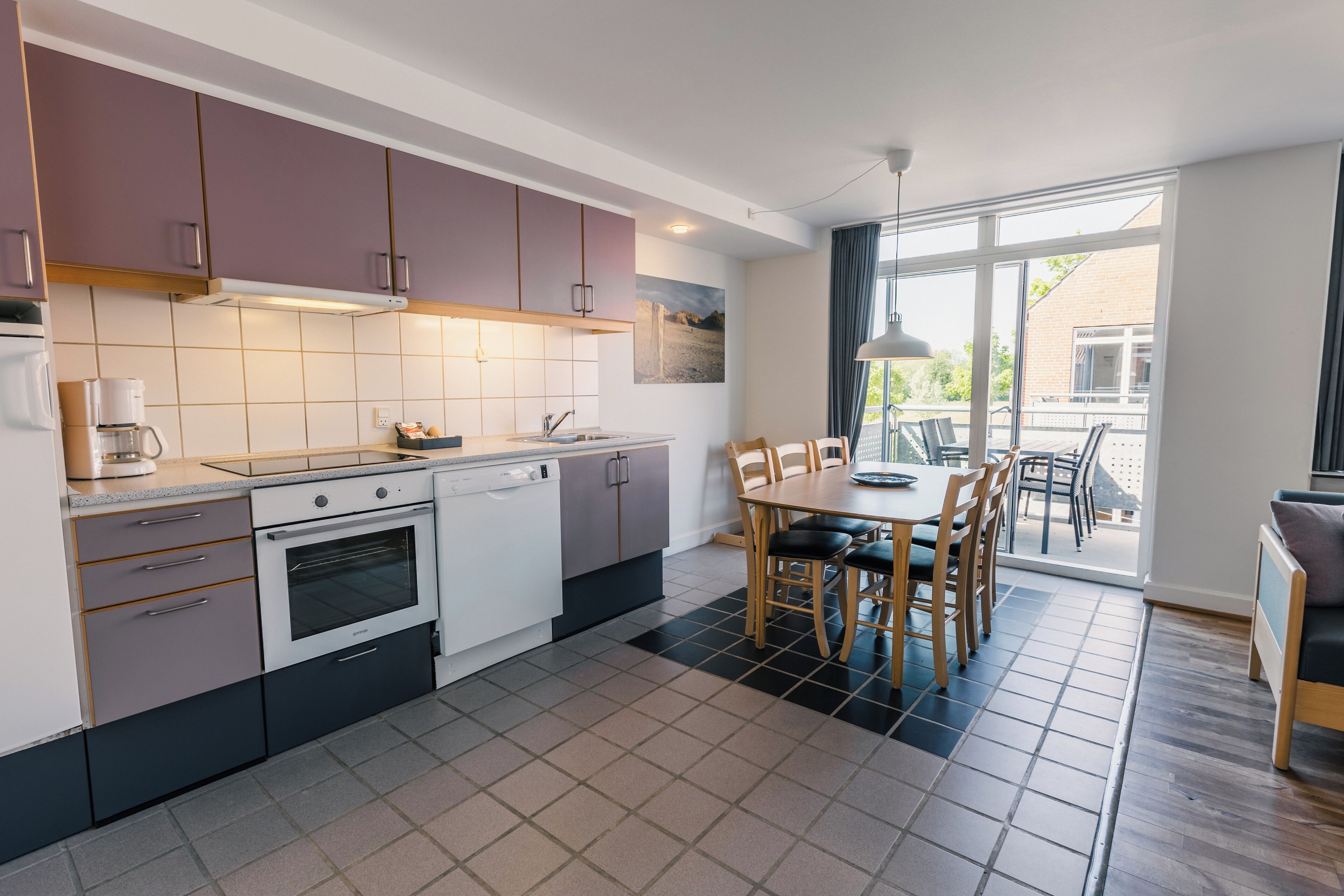 Una cocina moderna con comedor, que incluye lavavajillas, horno y un amplio ventanal con vistas a un balcón.