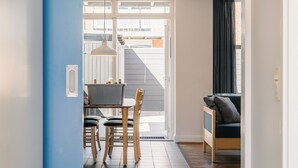 A hallway with a blue accent wall, a dining area with a table and chairs, and a sofa in a room with a view through a glass door.