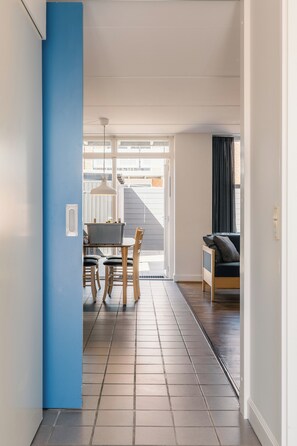 A hallway with a blue accent wall, a dining area with a table and chairs, and a sofa in a room with a view through a glass door.