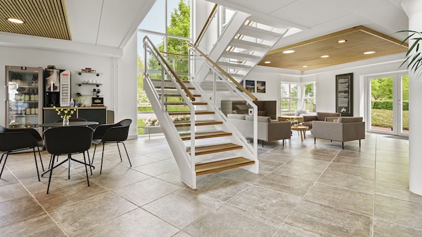 A spacious living area with a central staircase, a dining area with chairs and a table, and a kitchen with appliances and shelves. - Ribe Byferie Resort (Ribe)