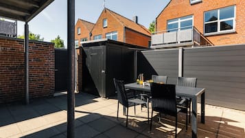 Een terras met een tafel, stoelen, een tuinhuisje en een bakstenen muur.