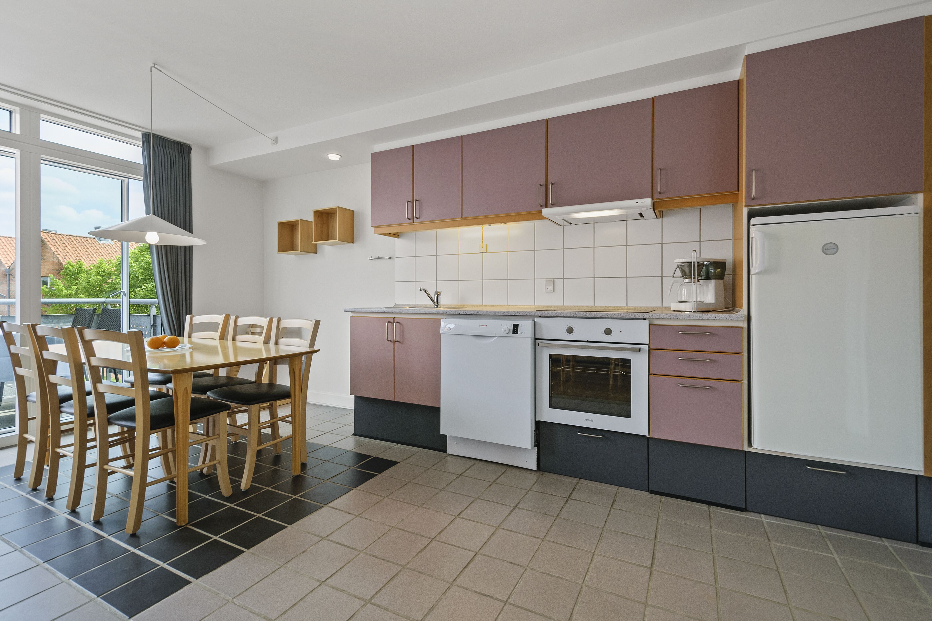 A modern kitchen with a dining area, featuring a dishwasher, oven, and a refrigerator.