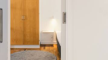 A hallway with a wooden wardrobe, a small table with a lamp, and a grey rug on a wooden floor.