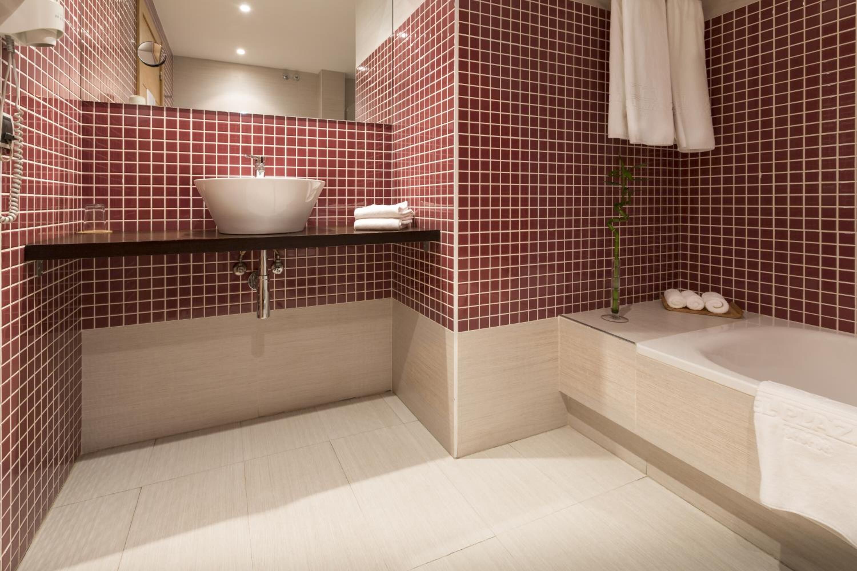 Un bagno con un lavandino bianco, una vasca e pareti rivestite di piastrelle rosse.