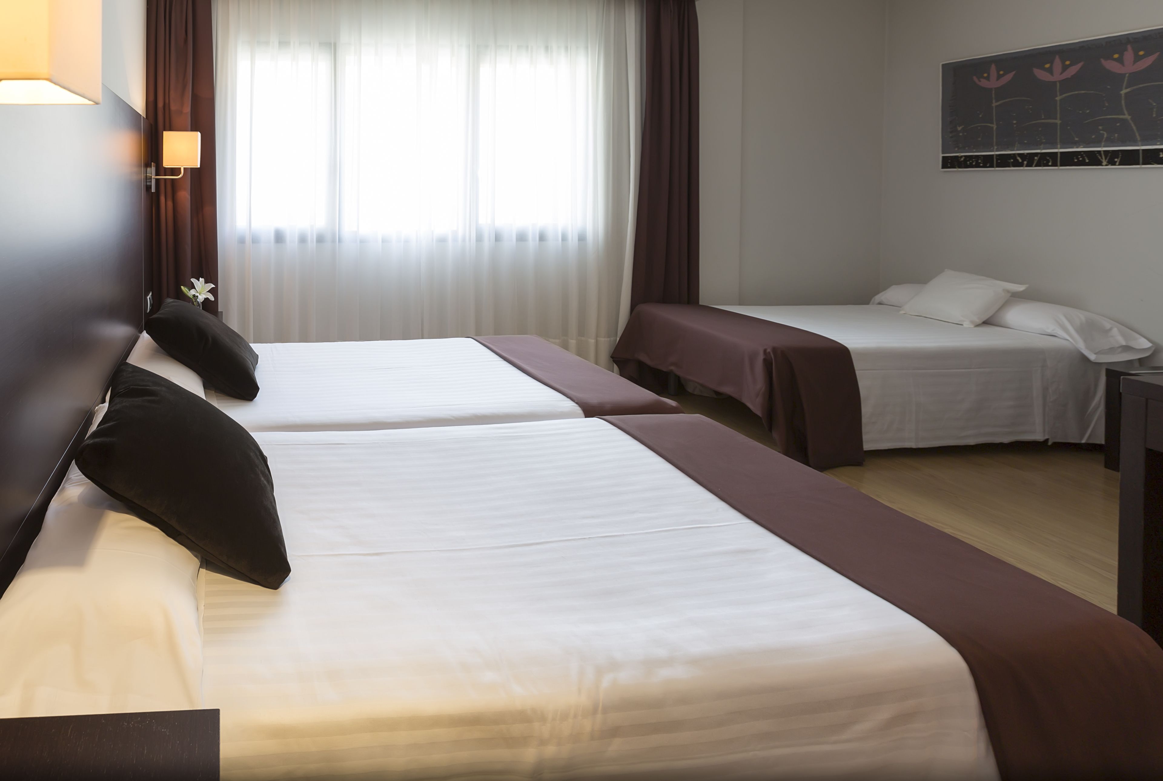 Ein Hotelzimmer mit zwei Betten, einem Nachttisch, einer Lampe und einem Fenster mit Vorhängen.