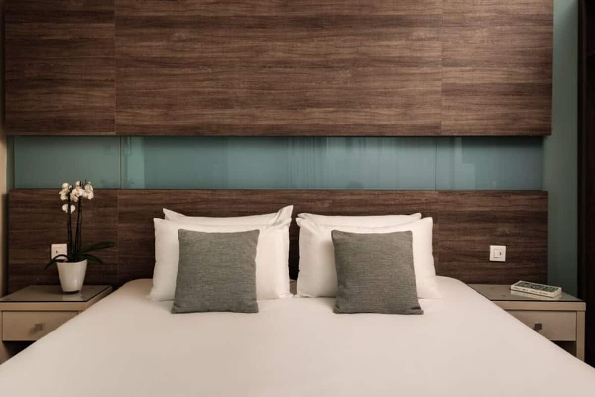 A hotel room with a large bed, two nightstands, a potted plant, and a wooden headboard.