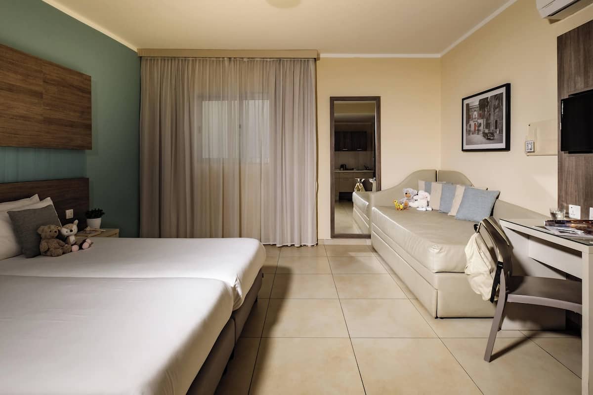 A hotel room with a bed, a desk, a chair, a sofa, and a bathroom visible through an open door.