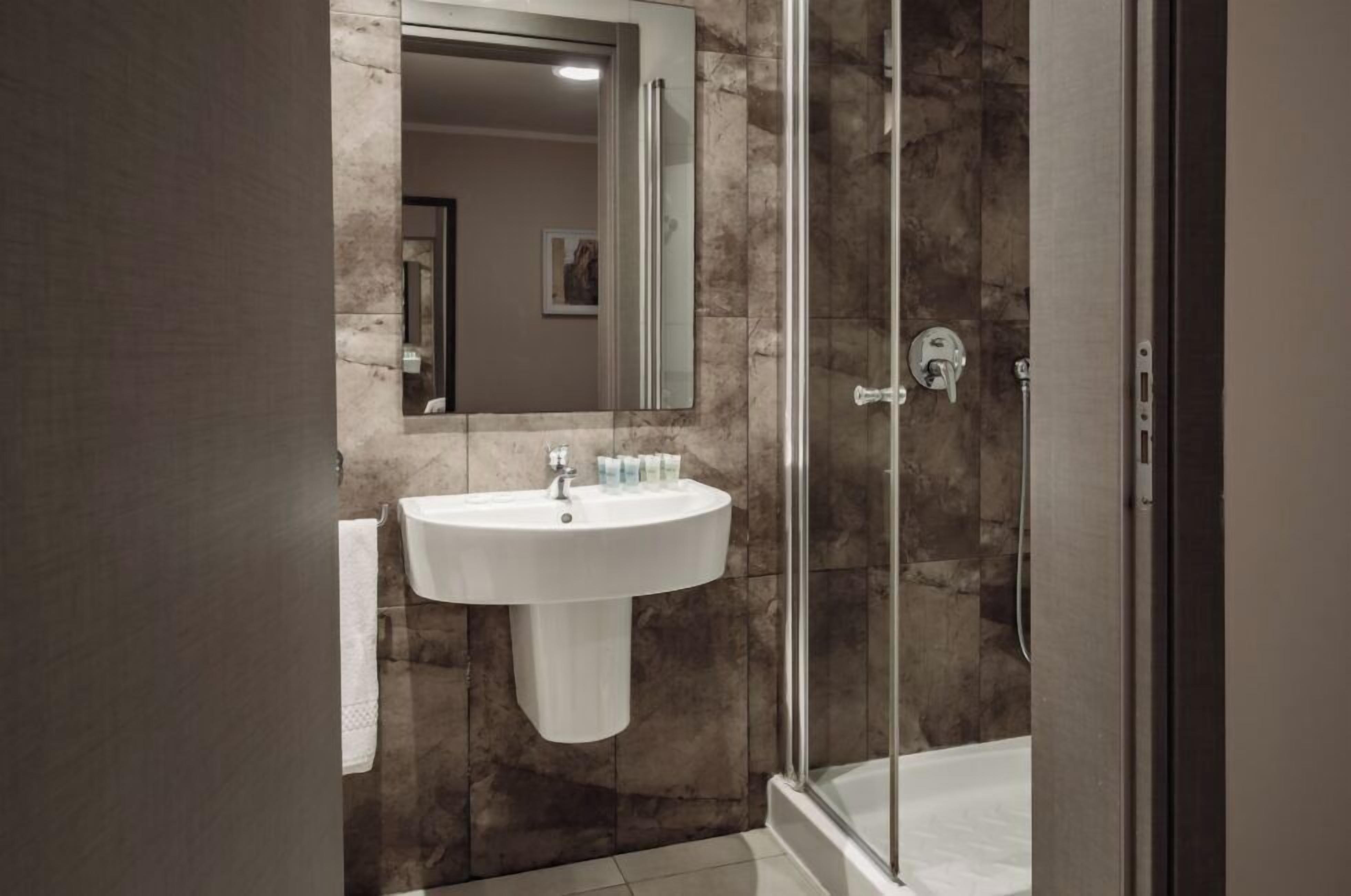 Un baño moderno con pared de mármol, un lavamanos blanco y una cabina de ducha de vidrio.
