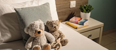 A bed with two teddy bears, a pillow, a bedside table with a plant, and a book.