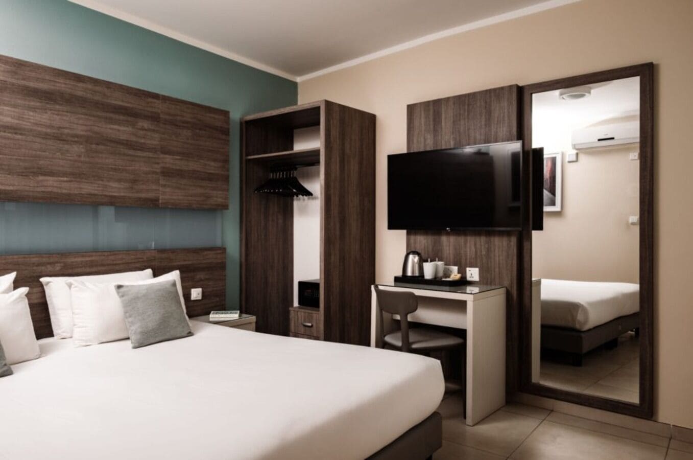 Ein modernes Hotelzimmer mit einem großen Bett, einem Schreibtisch, einem Fernseher und einem Kleiderschrank.