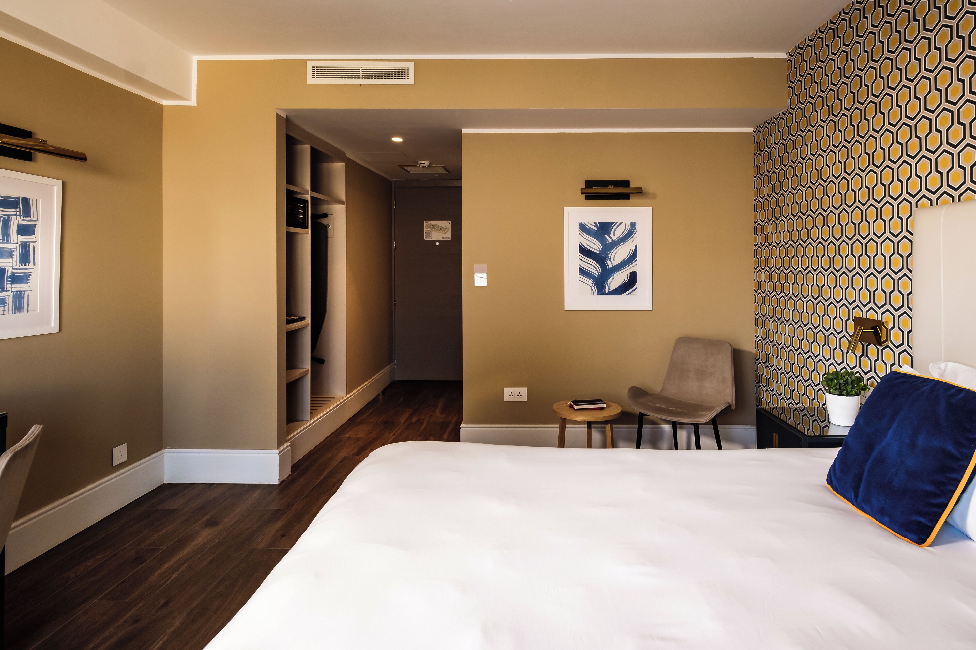 A hotel room with a large bed, a chair, a small table, and a wardrobe.