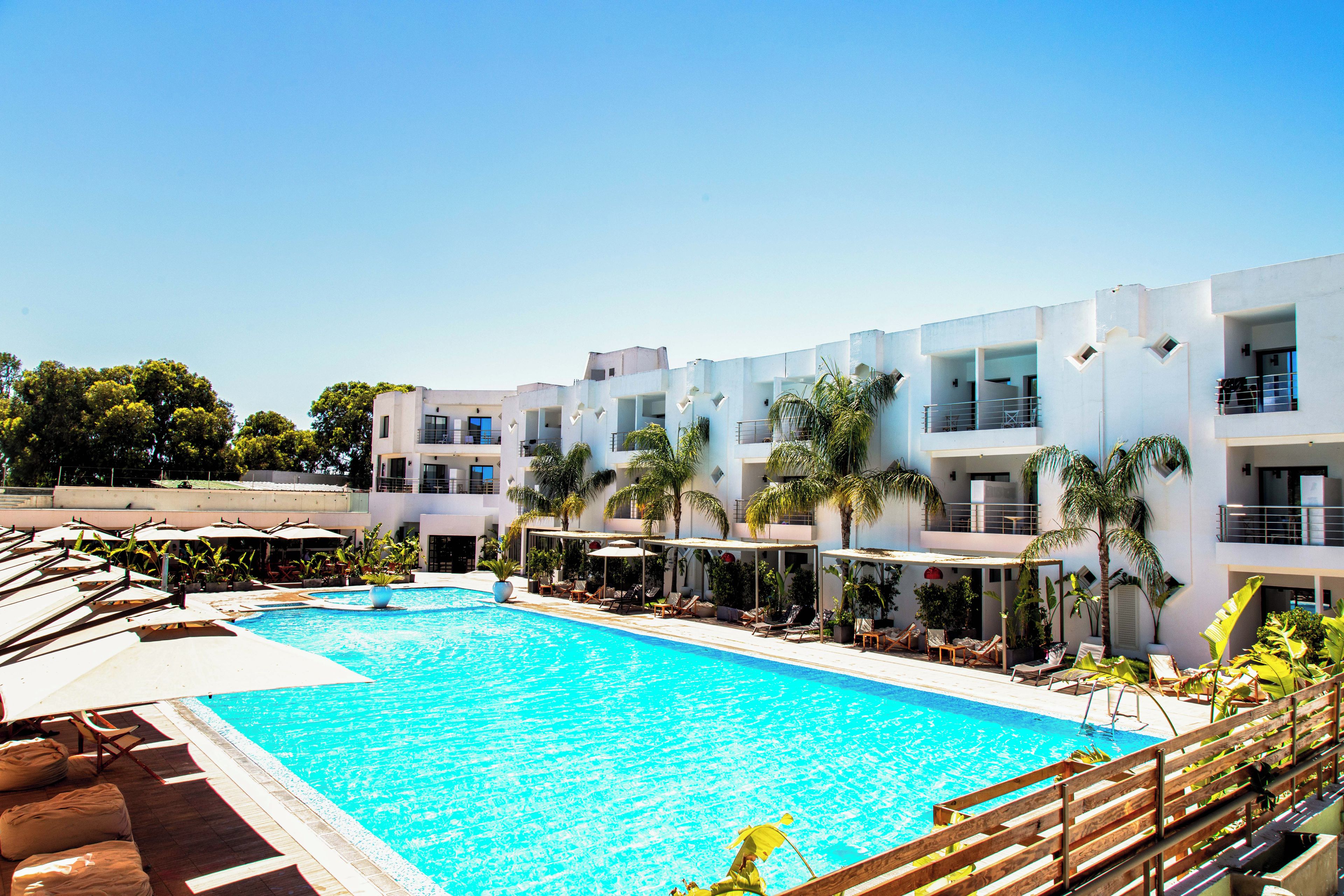 Un hotel moderno con piscina, varios balcones y zonas de estar al aire libre.