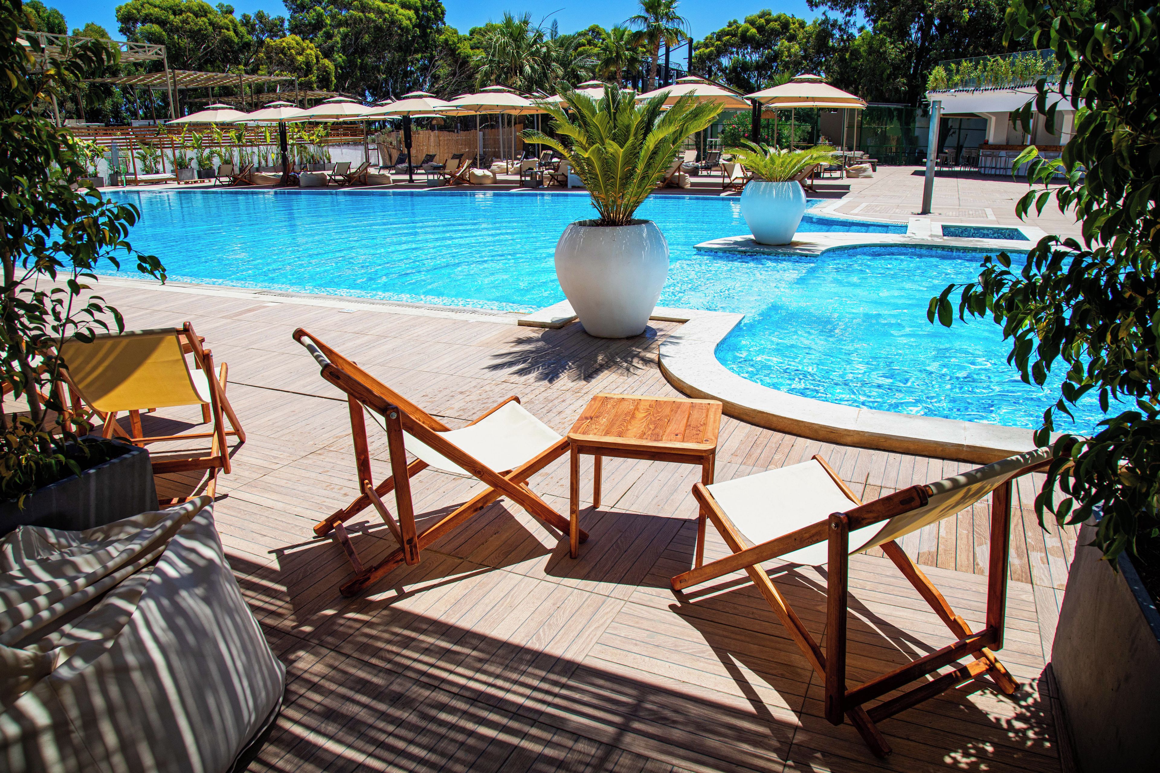 Un espace aménagé au bord de la piscine, avec des chaises longues et des parasols, entouré d’une végétation luxuriante.