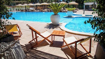 Un espace aménagé au bord de la piscine, avec des chaises longues et des parasols, entouré d’une végétation luxuriante.