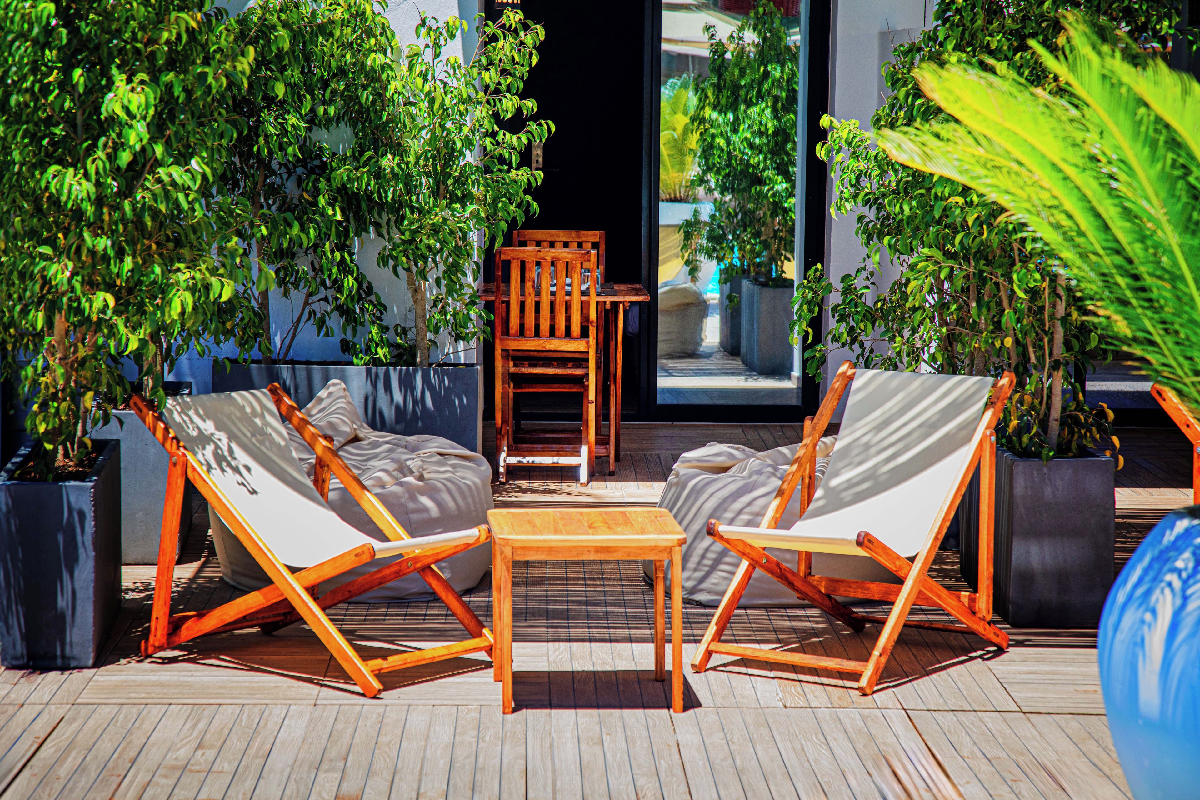 A deck with two wooden chairs and a table, surrounded by potted plants.