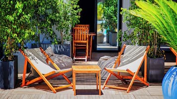 Una terraza con dos sillas y una mesa de madera, rodeada de plantas en macetas.