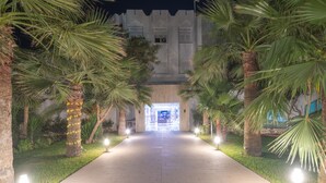 Un chemin menant à un bâtiment à l’architecture moderne, entouré de palmiers et illuminé par des jeux de lumière.