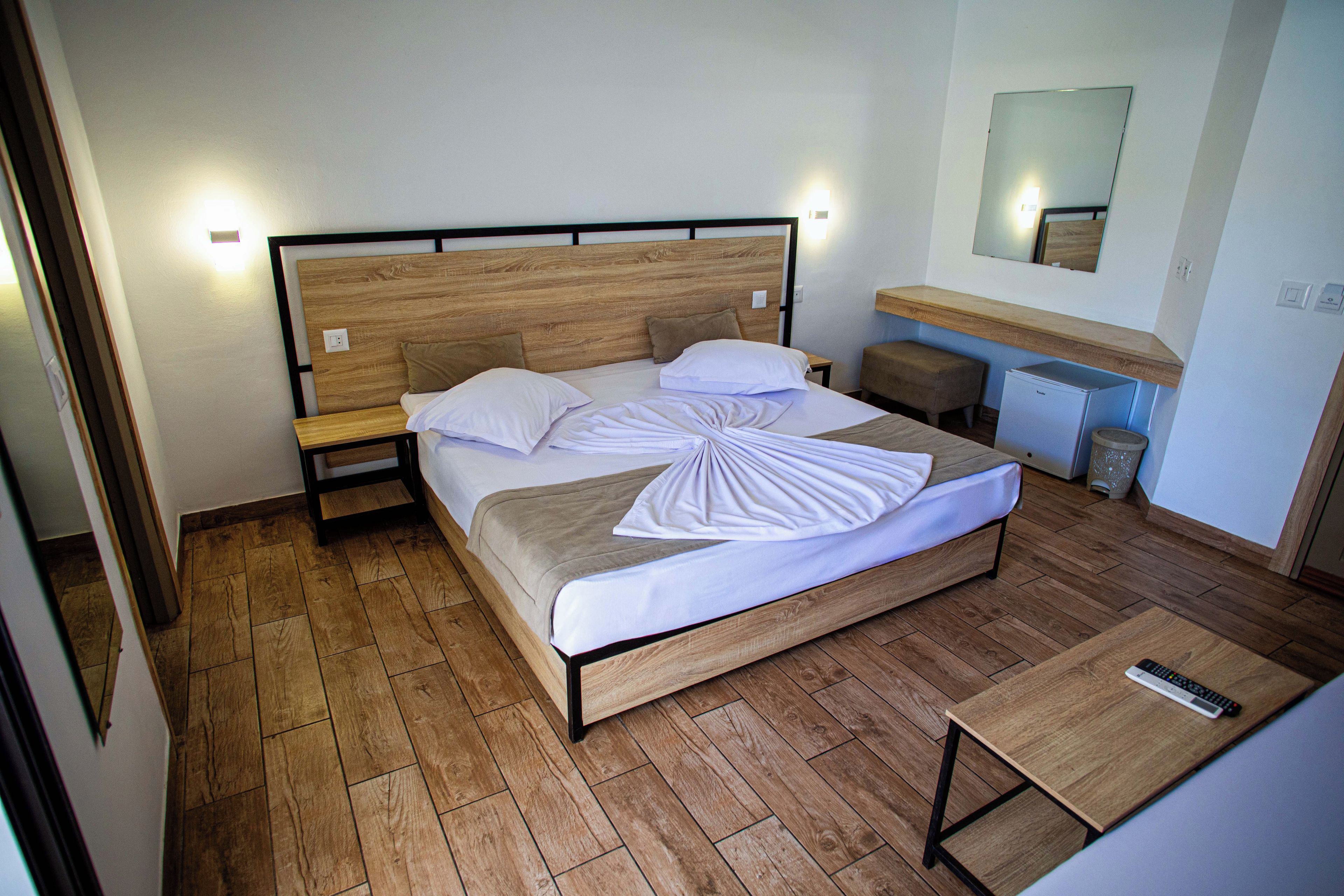 Une chambre d’hôtel avec un lit en bois, des tables de chevet, un bureau, une chaise, un miroir et un petit réfrigérateur.