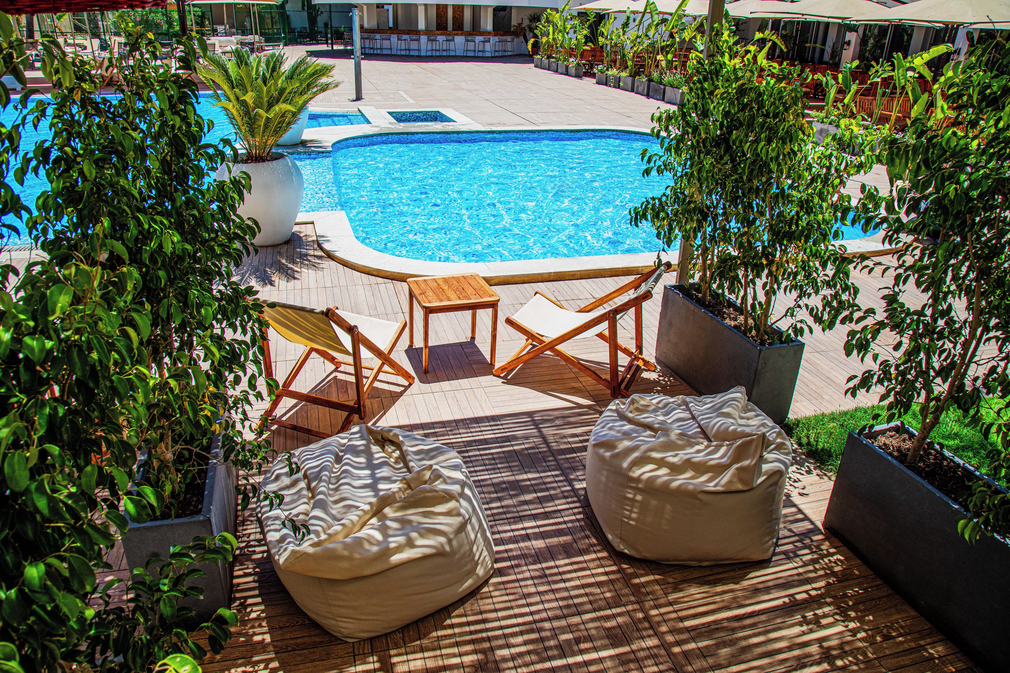 A poolside area with a pool, wooden deck, lounge chairs, and potted plants.