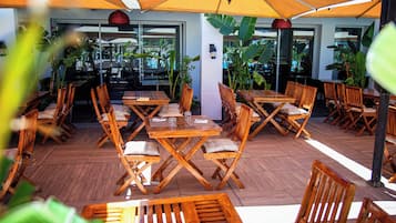 Un espace extérieur aménagé avec des tables et des chaises en bois, entouré de grands parasols et de plantes en pot.