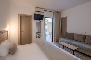 Habitación de hotel con cama, sofá, televisión y puerta corredera que da a un espacio exterior.