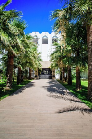 A pathway lined with palm trees leading to a building with a modern architectural style. - Acqua Viva Village (La Marsa)