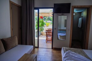 A hotel room with a sofa, a bed, a TV mounted on the wall, and a sliding door leading to an outdoor area with a chair and plants. - Acqua Viva Village (La Marsa)
