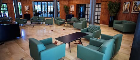 A lobby with green upholstered seating, a central table, and large windows.