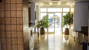 A spacious lobby with a tiled wall, a reception desk, and two large potted plants. - Hotel Emira (Hammamet)
