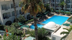 A resort with a large pool, palm trees, and a view of the sea. - Hotel Emira (Hammamet)