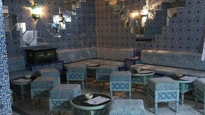 A room with patterned walls, a seating area with cushioned chairs and tables, and decorative wall sconces. - Hotel Emira (Hammamet)