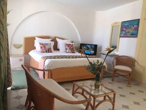 A hotel room with a bed, a television, a mirror, and two wicker chairs. - Djerba Orient (Mezraia)
