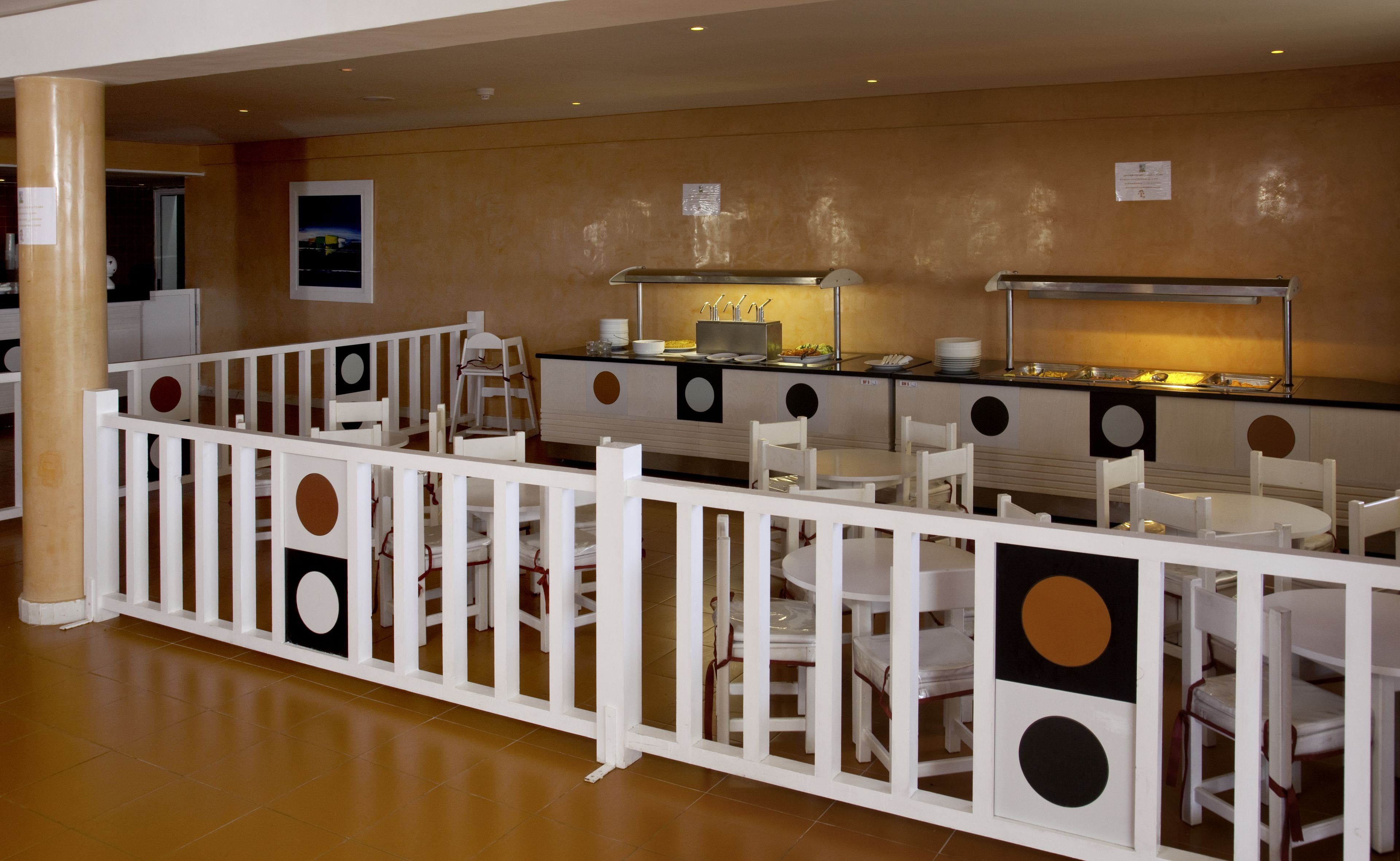 A buffet area with white tables and chairs, a white fence, and a buffet counter with various food items.