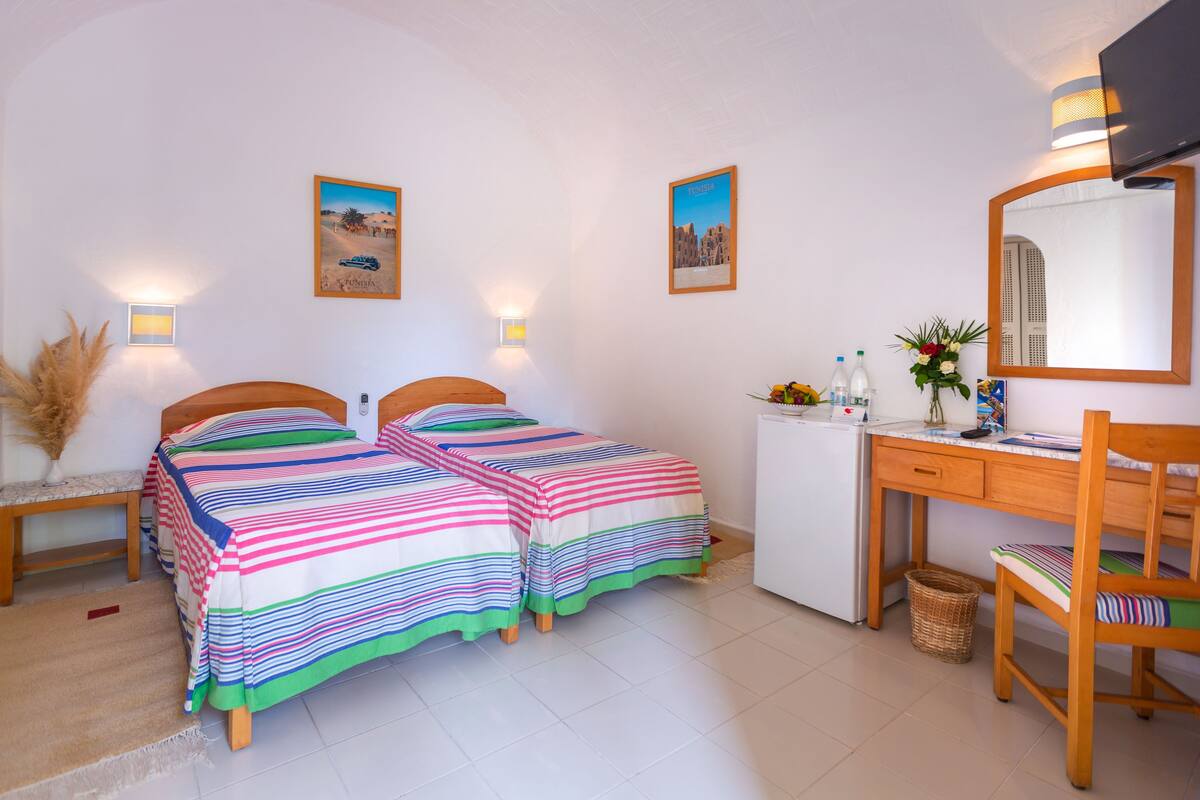 A hotel room with two beds, a desk, a small refrigerator, and a mirror.