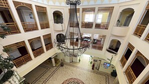 A multi-level atrium with a central chandelier, multiple balconies with wooden railings, and a patterned floor design.